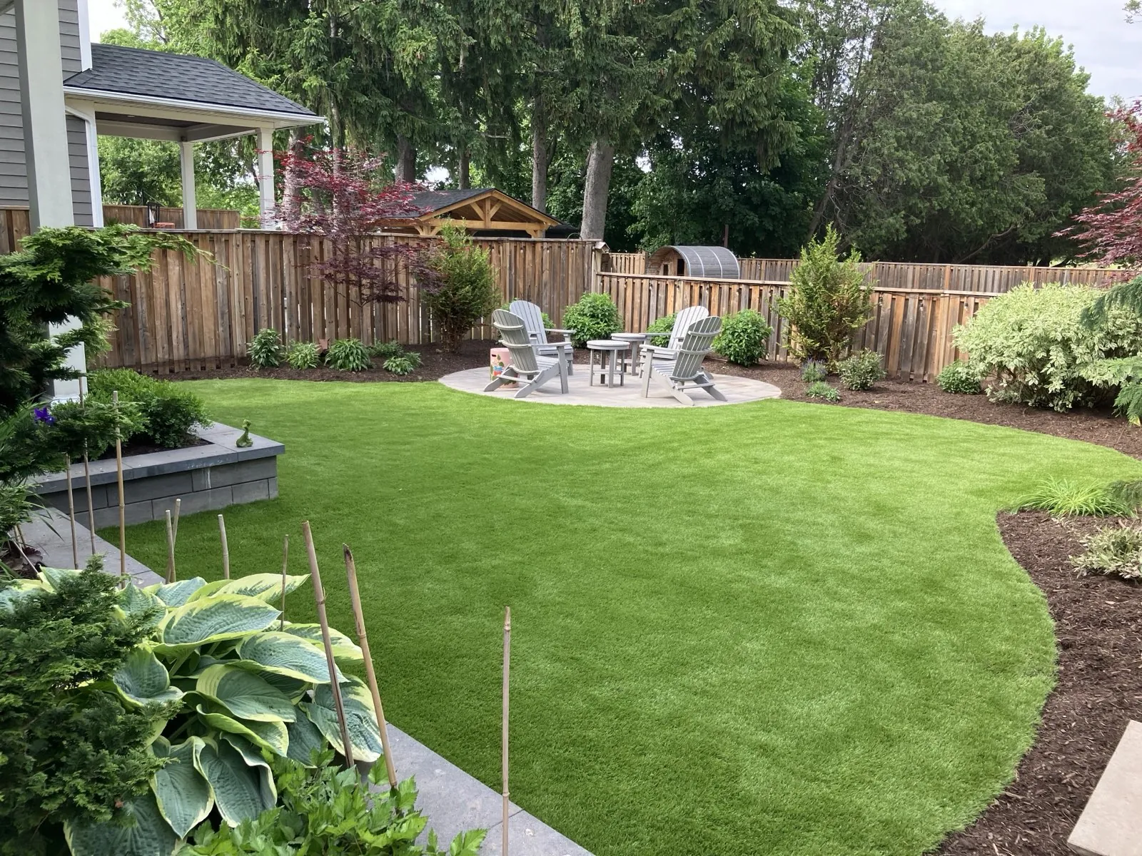 Lush green backyard lawn curving around a paver patio with pergola seating and layered garden beds, landscaped by Walnut Creek in Hamilton, Ontario