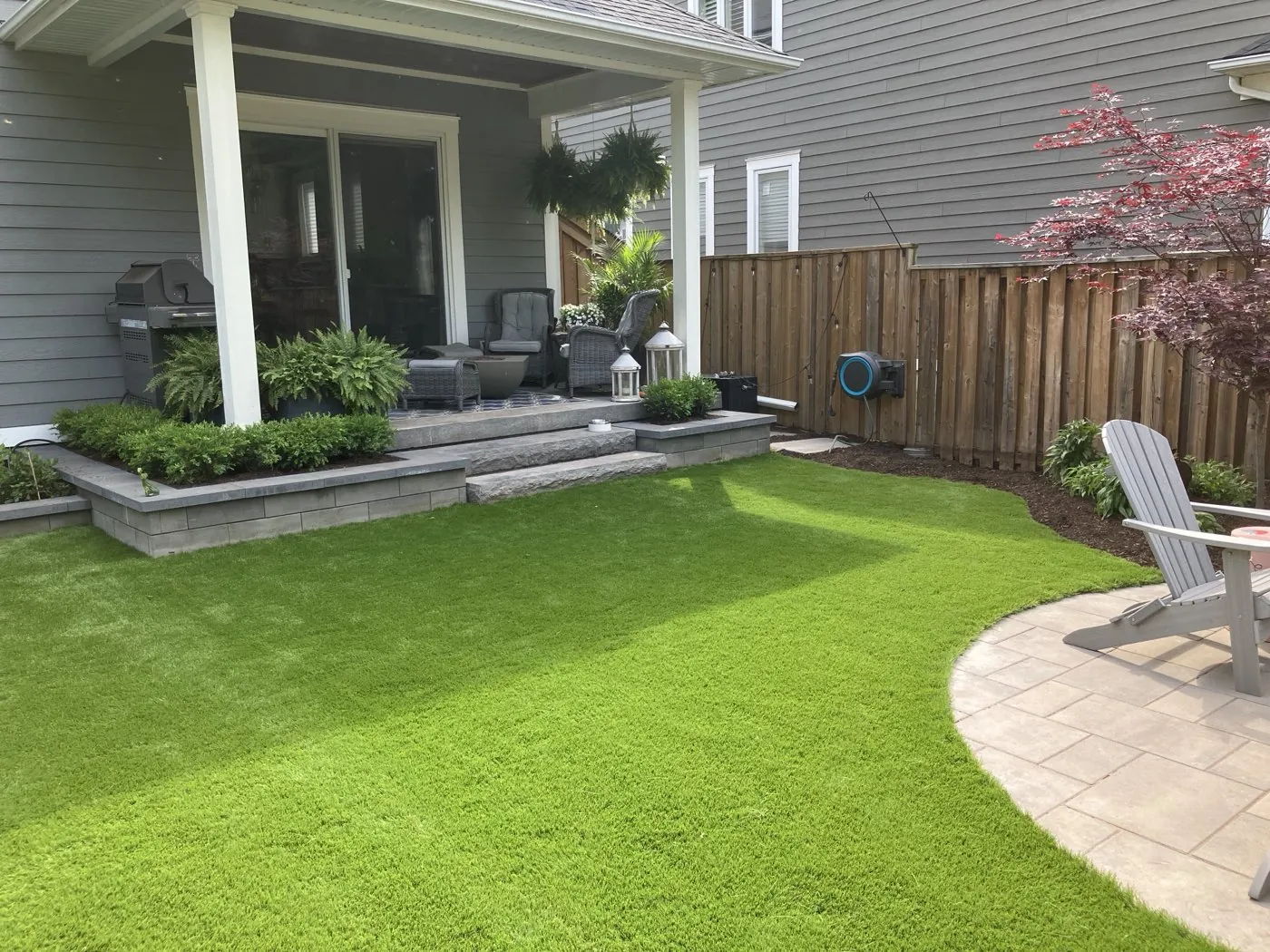 Lush backyard lawn with a raised paver patio, pergola and lounge seating in a Hamilton backyard