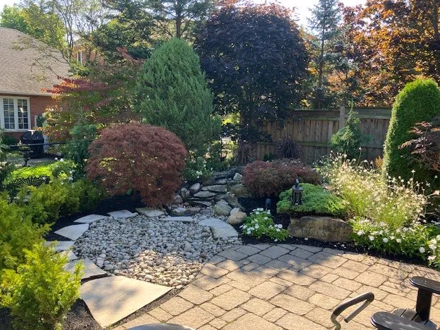 Backyard rock garden with a red Japanese maple, river-rock bed and flagstone patio in Hamilton