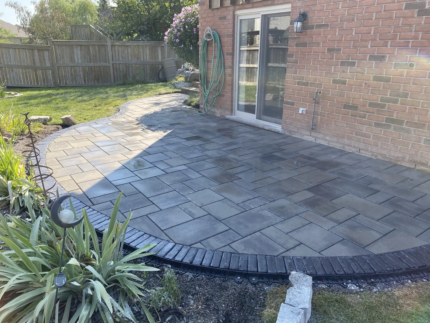 Charcoal paver patio with a curved border behind a brick home in Hamilton