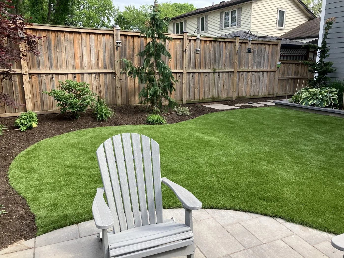 Manicured backyard lawn curving around a paver patio with a Muskoka chair, framed by a privacy fence in Hamilton