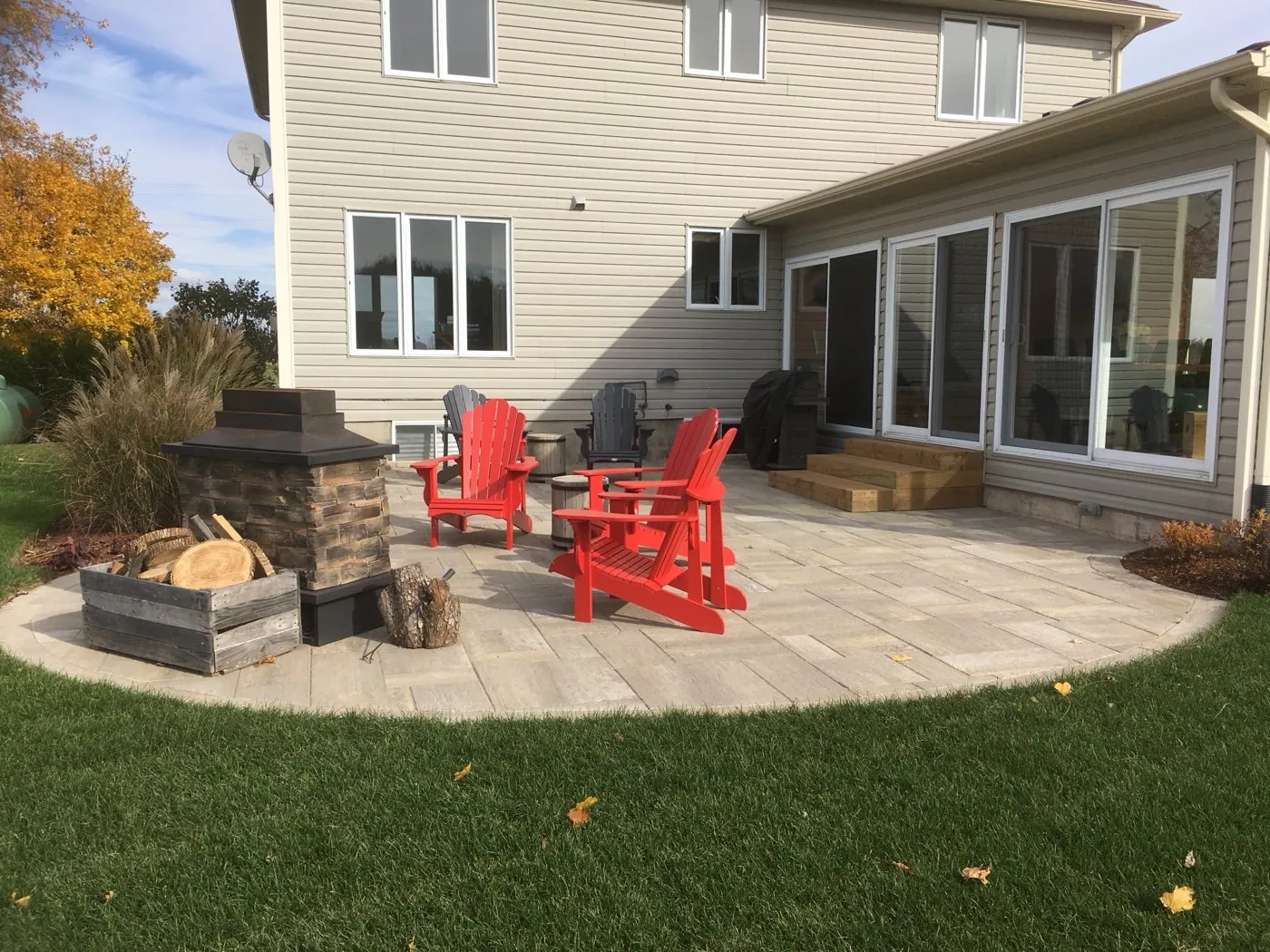 Paver patio with a stone fire feature and red Muskoka chairs behind a two-storey home in Hamilton