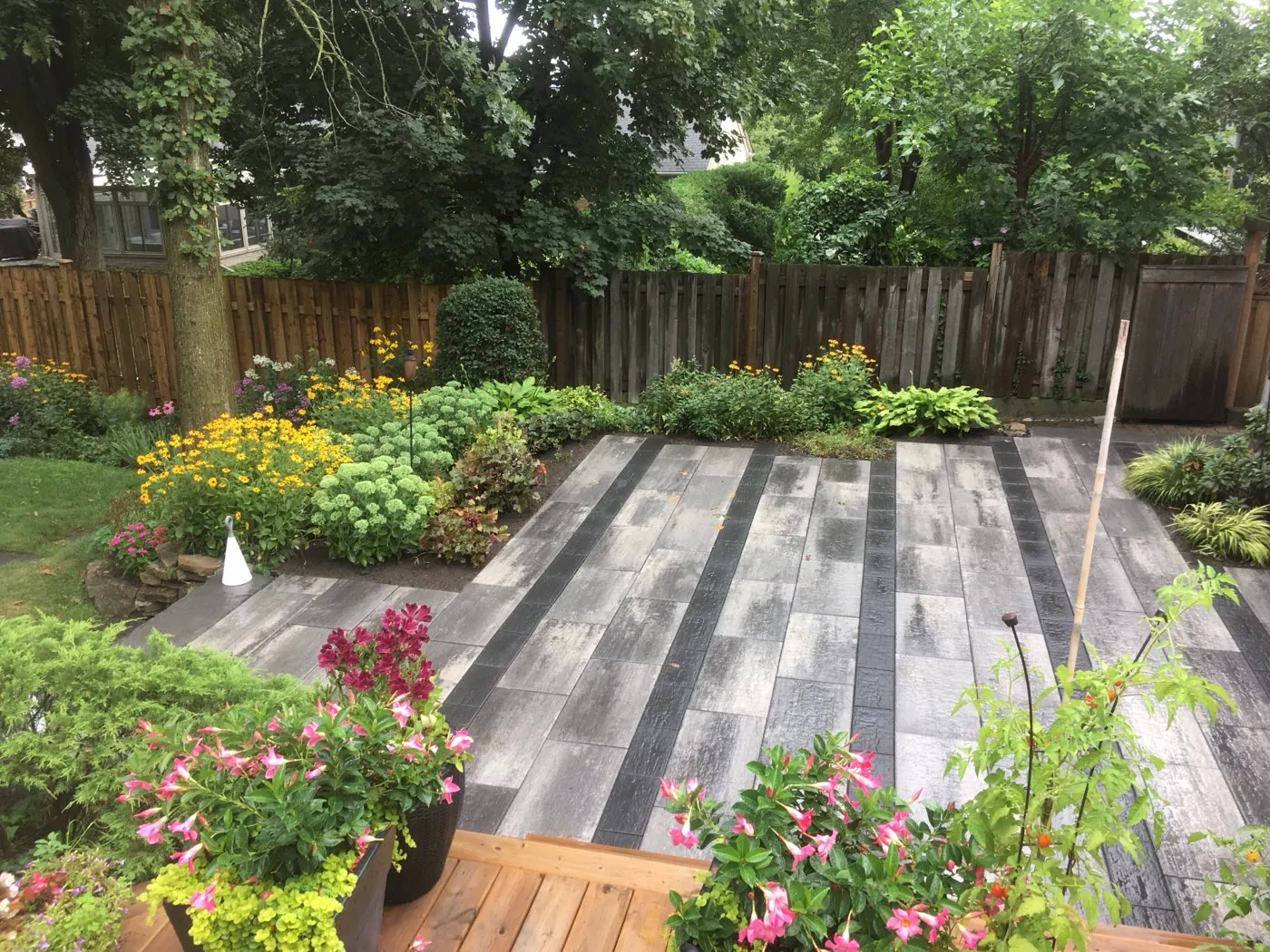 Grey plank-paver patio bordered by lush perennial gardens and potted flowers in a Hamilton backyard