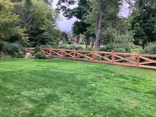 Post-and-rail wood fence bordering a lush, mature lawn with mature trees in Hamilton